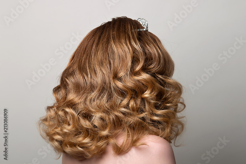 Female hairstyle long curls on the head of the brown-haired woman looking back at the gray background turning the head to the right.