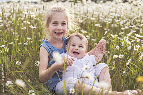 Cute child girl at camomile field daisy with baby brother