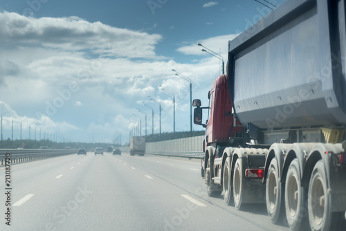 Tipping lorry driving on the asphalt road in the rural landscape. sky with clouds photo