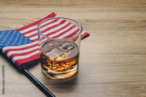 close up of a glass of bourbon whiskey and the flag of the United States of America on wooden table