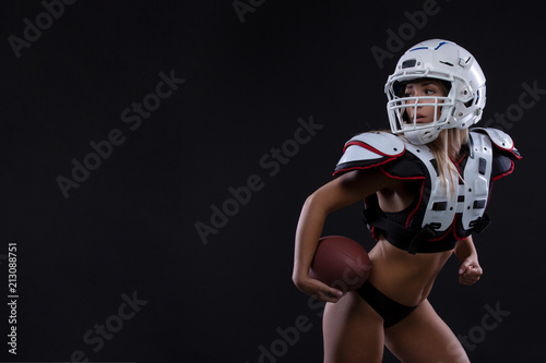 Sportive serious woman in helmet of rugby player holding ball in stuio on dark background. . Copy space