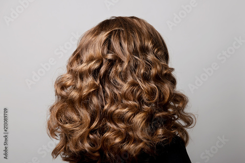 Female hairstyle long curls on the head of the brown-haired woman back view at the gray background turning the head to the right. photo