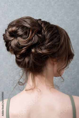 Female hairstyle is a high bun of a rear view on a gray background.