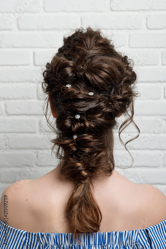 Female hairstyle Greek braid on the head of a brunette rear view.