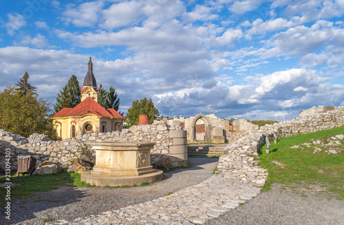 Bilde på lerret Medieval ruins of castle walls and a well with a church in the background in Mis