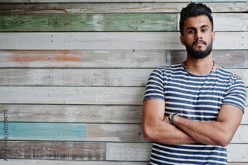 Handsome tall arabian beard man model at stripped shirt posed outdoor against wooden background. Fashionable arab guy.