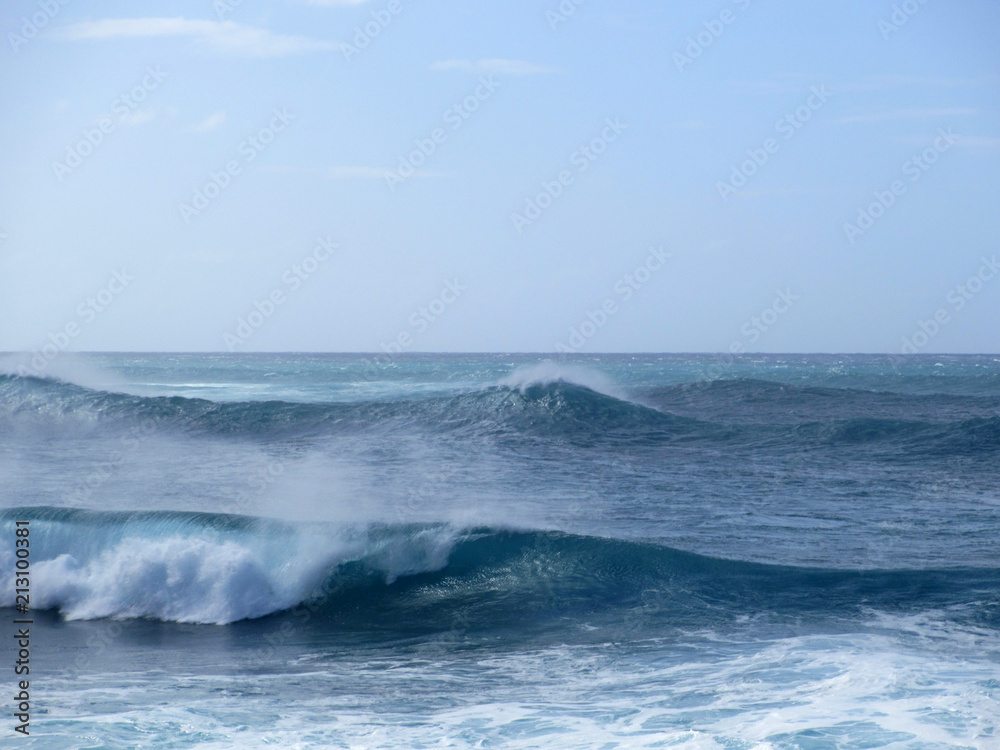 Waves break and crash towards the shore with dramatic blue sky