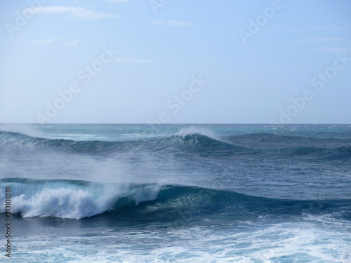 Waves break and crash towards the shore with dramatic blue sky