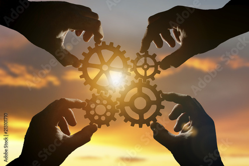 Four hands of businessmen collect the gear from the gears of the details of the puzzles. against the background of sunlight. Concept business idea. Teamwork, cooperation, strategy