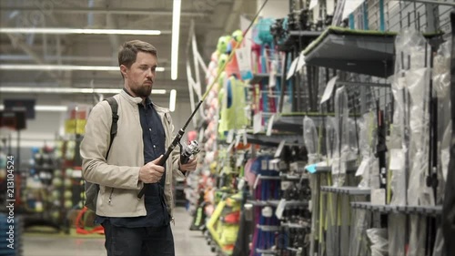 Casual adult guy wants to buy new equipment for fishing. Man holding new fishing pole, spinning gears, checks the quality. Ready for fishing. photo