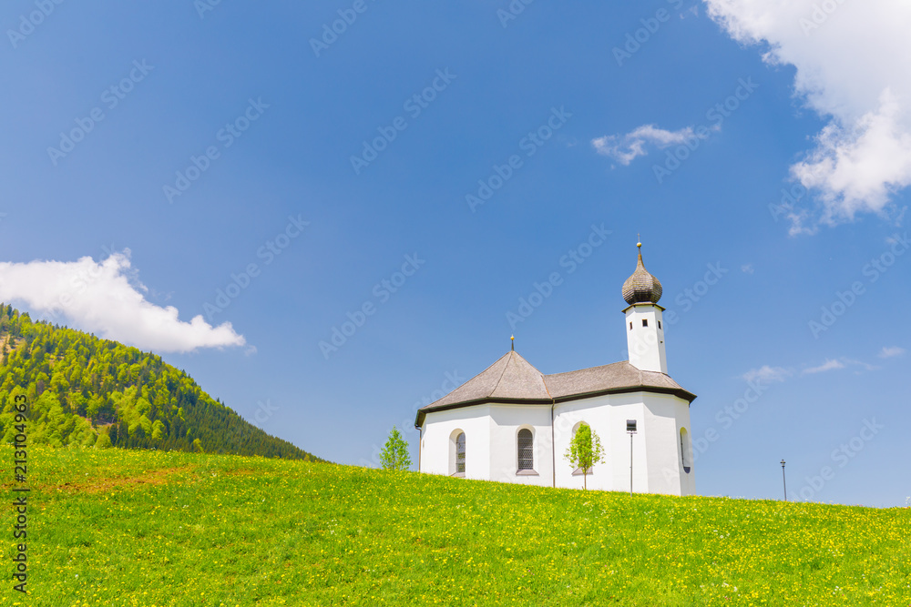 Chapel Sankt Anna in Achenkrich on a spring day with meadow of yellow flowers