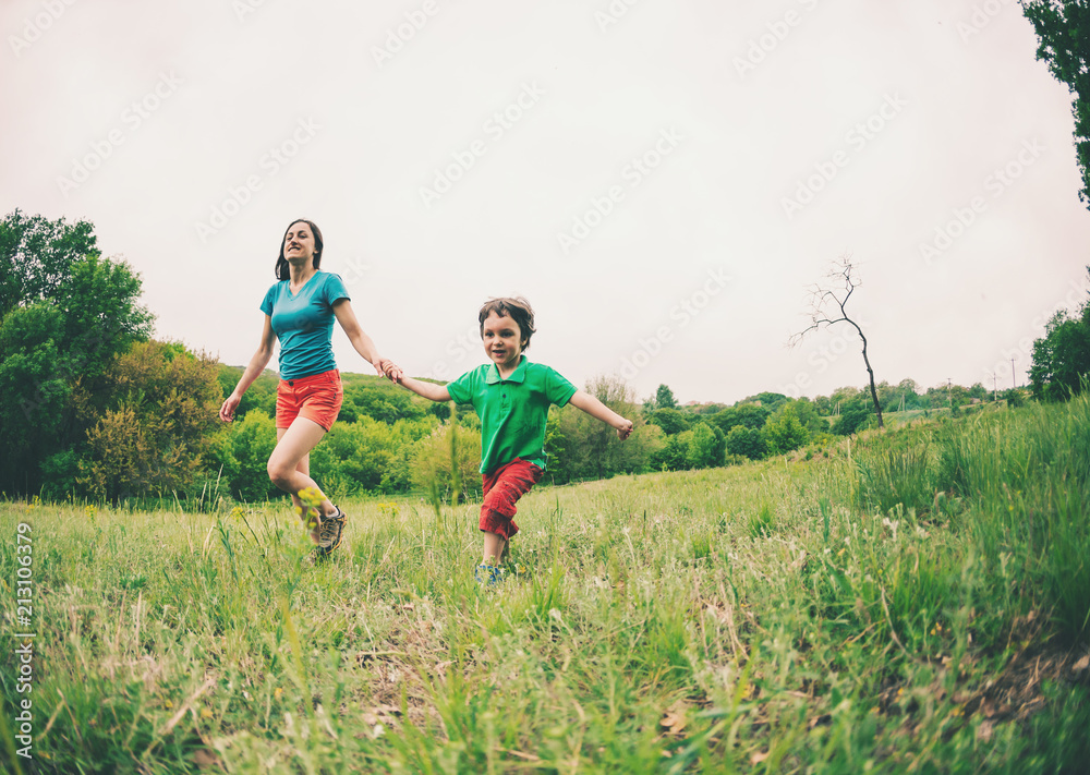 A woman and her son are running along the grass.
