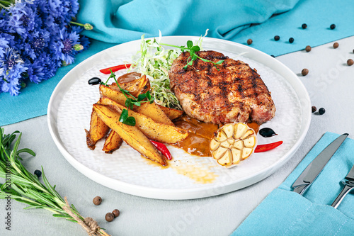 Fried steak and vegetables on the grill on a plate closeup view. Meat with potatoes, garlic, tomato, microgrin. French cuisine photo