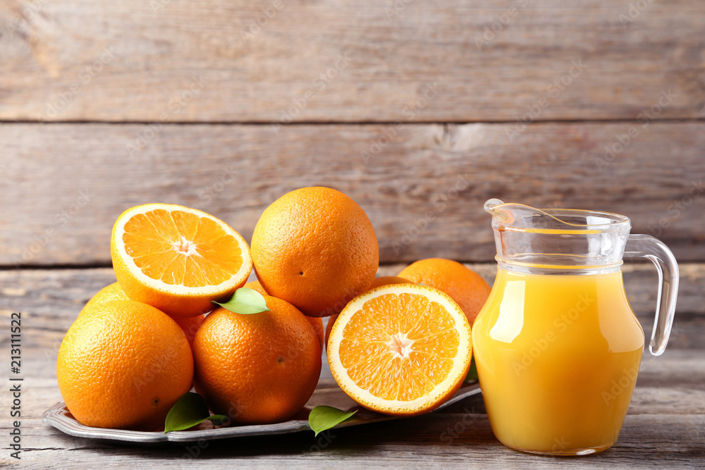 Orange fruit in tray with jug of juice on grey wooden table Orange fruit in tray with jug of juice on grey wooden table