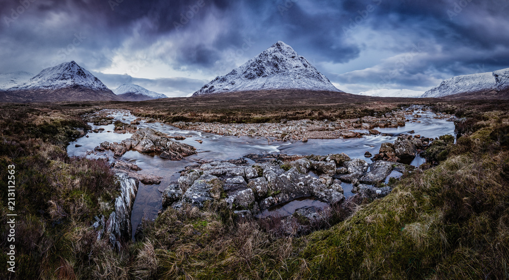 Panorama photo from Scotland. Amazing natural landscape, snow covered mountain, river and rough rocky shore. Beautiful place to unwind. Great for adventurous holiday.