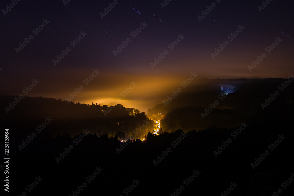 Mystical night photo of landscape with only some light from valley below being held by low clouds and fog. Dramatic, exciting, adventure, night, calm, quiet.
