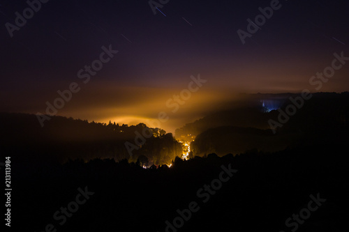 Mystical night photo of landscape with only some light from valley below being held by low clouds and fog. Dramatic, exciting, adventure, night, calm, quiet.