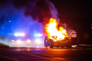 Car on fire at night with police lights in background