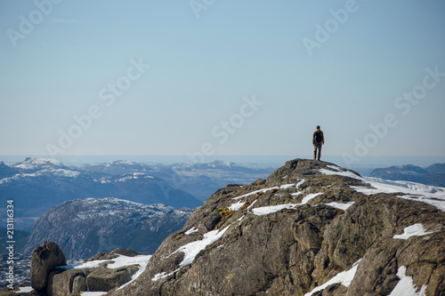 Rear view of hiker man standing on the Preikestolen rocks and looking at the beautiful mountains. Sunny winter day in Norway photo
