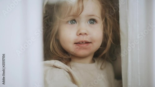 Happy little girl with rush, look and wave through the window smiling. Handheld