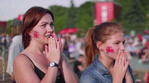Girls with Britain flag on cheeks watch football match in fan zone