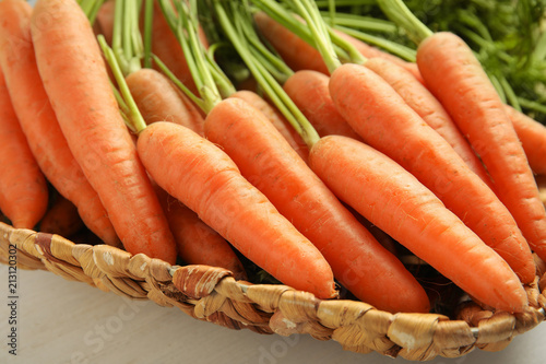 Wicker tray with ripe carrots on table, closeup