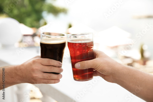 Friends clinking glasses with tasty beer outdoors