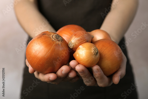 Woman holding ripe onions on grey background