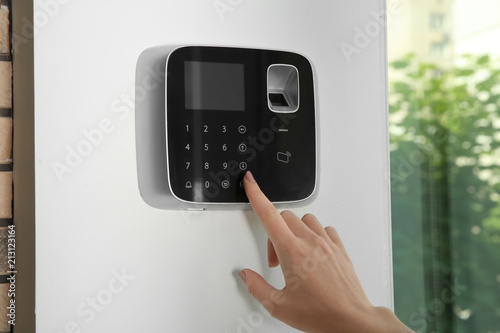 Young woman entering code on alarm system keypad indoors
