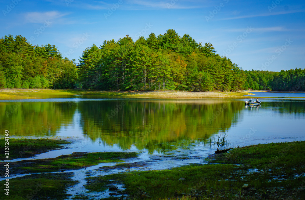 Reflection on lake with small visible fishing boat with 2 men fishing