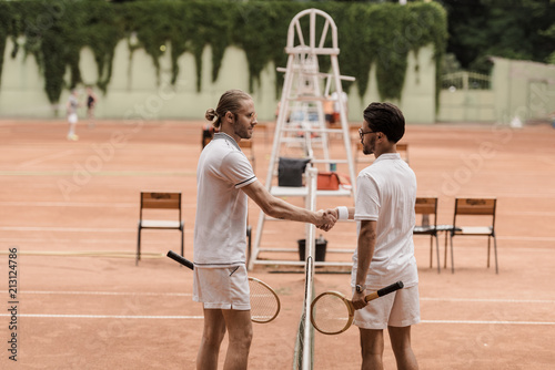 side view of retro styled tennis players shaking hands above tennis net at court