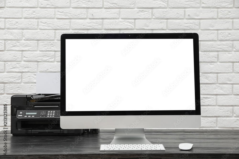 Fototapeta premium Computer on desk against brick wall in home office. Comfortable workplace