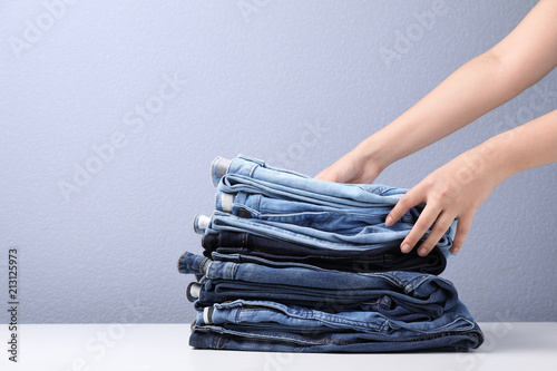 Young woman folding stylish jeans on table