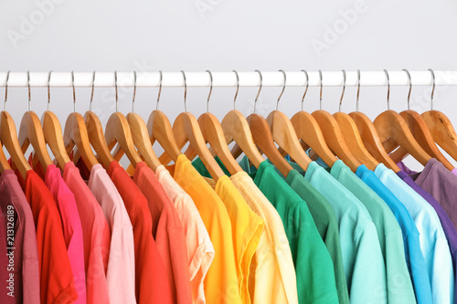 Rack with rainbow clothes on light background