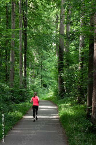 Young woman running along path through green forest.