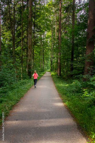 Young woman running along path through green forest. © Simon