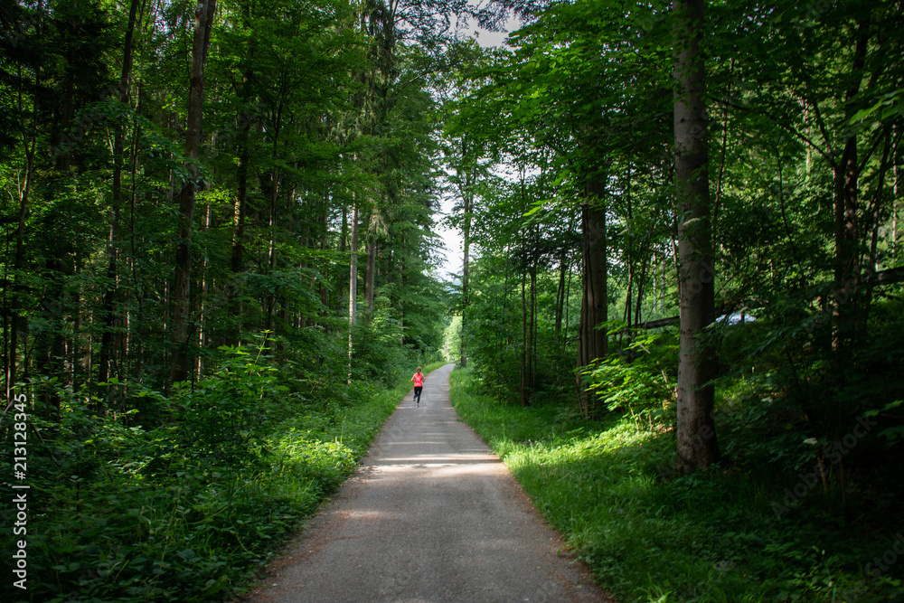 Fototapeta premium Young woman running along path through green forest.