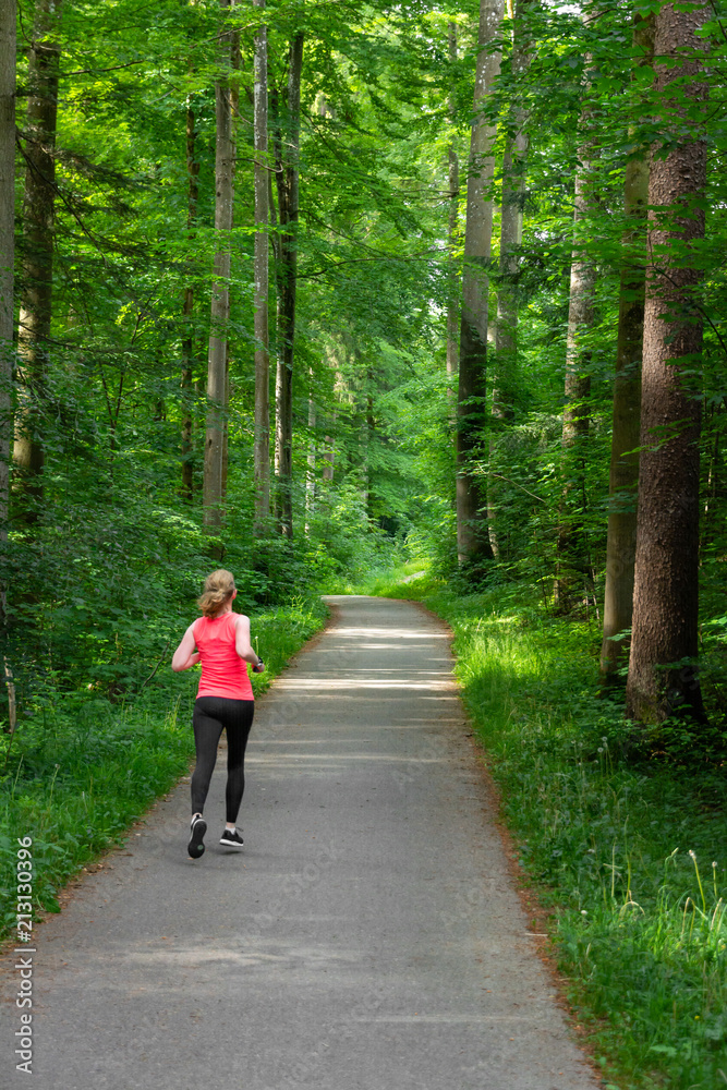 Young woman running along path through green forest. Young woman running along path through green forest.
