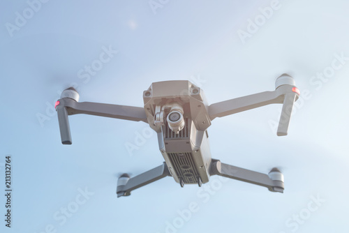 Flying quadrocopter drone in the air under blue sky with lens flare. 