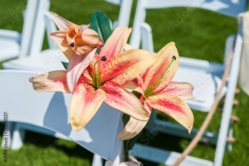 Pink and orange Stargazer lily flowers embellish  the white rows of chairs at the wedding ceremony venue. photo