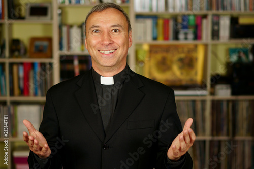 A good looking smiling catholic priest is openning his arm to us. He looks at us with interest, pensiveness, proselytising, joy and happiness. photo