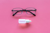 Eye drops in small bottle near glasses on pink background top view space for text
