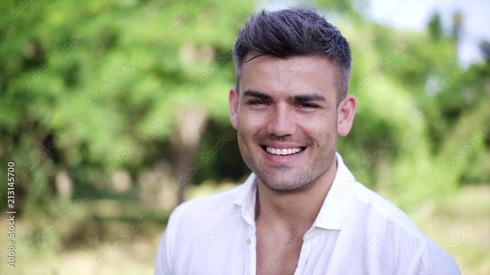 Portrait of a attractive man smiling showing white teeth looking at camera and a perfect physical and combed hair. Concept of: health, fitness, beauty. Summer green background Portrait of a attractive man smiling showing white teeth looking at camera and a perfect physical and combed hair. Concept of: health, fitness, beauty. Summer green background