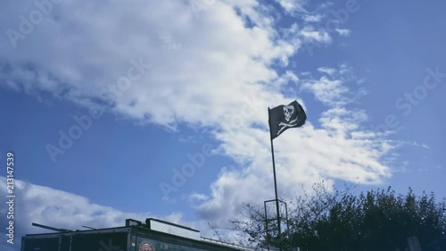 Black pirate flag flutter on wind with partly overcast blue sky. Jolly Roger sign on building inland. photo