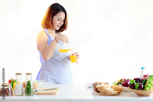 Charming pregnant beautiful woman is pouring orange juice into a glass at kitchen. Attractive mother has to take care herself for her baby. She looks happy and relaxed, isolated and white background