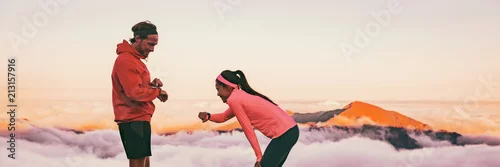 Obraz Biegacze zmęczeni oddychaniem po treningu patrzą na swój sportowy zegarek sportowy sprawdzający dane dotyczące tętna. Para dwóch sportowców biegnących razem w plenerze góry panorama banner.