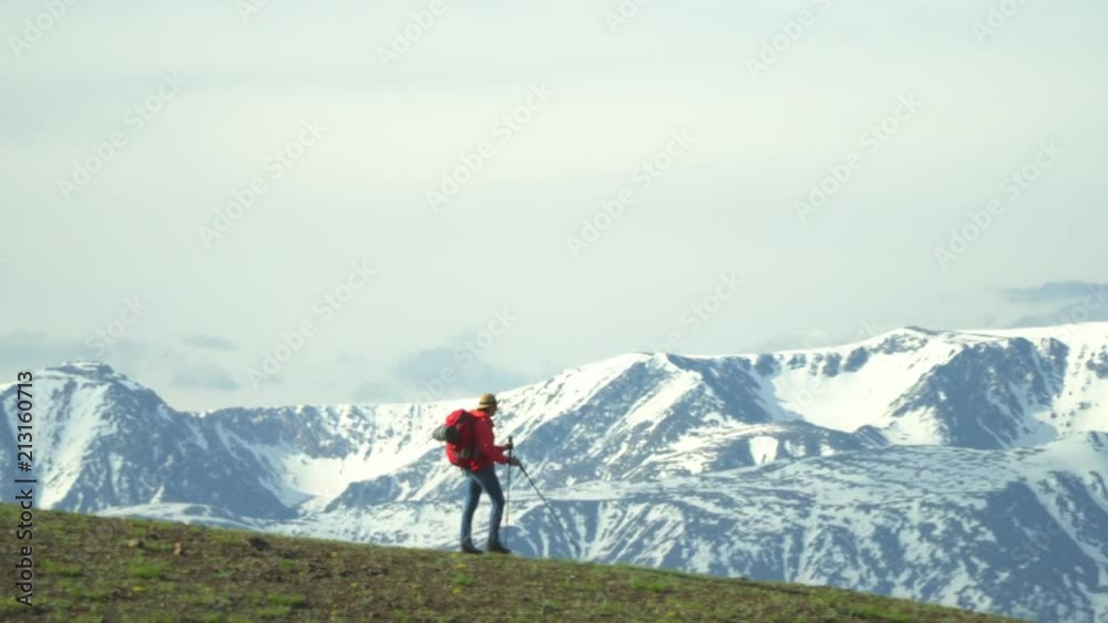 The woman the traveler climbs a mountain slope with sticks for tracking. Red backpack. Sticks for tracking. The woman the traveler climbs a mountain slope with sticks for tracking. Red backpack. Sticks for tracking.