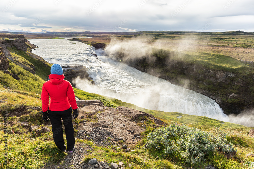 Iceland travel Gullfoss waterfall tourist woman looking over icelandic falls, famous attraction on the Golden circle. Nature lansdcape in summer, spring or autumn.