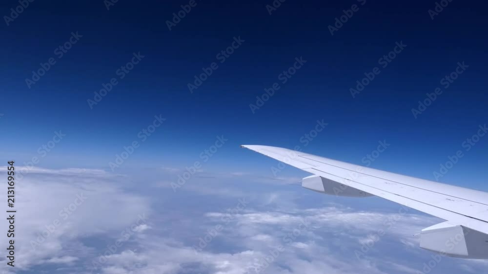 Airplane wing moving above white clouds under blue sky. Plane flight, view through window. Sunny day. Airplane wing moving above white clouds under blue sky. Plane flight, view through window. Sunny day.
