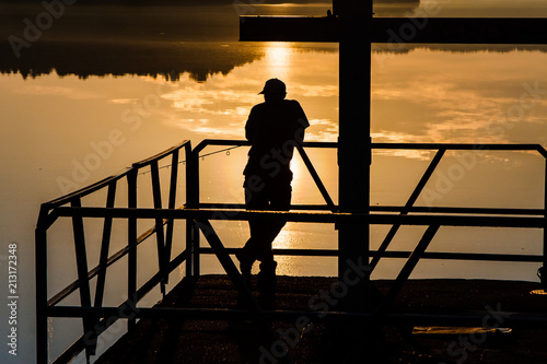 Experienced man fishing at sunset on the shore of peaceful lake. Sunset and sky reflection on the local lake